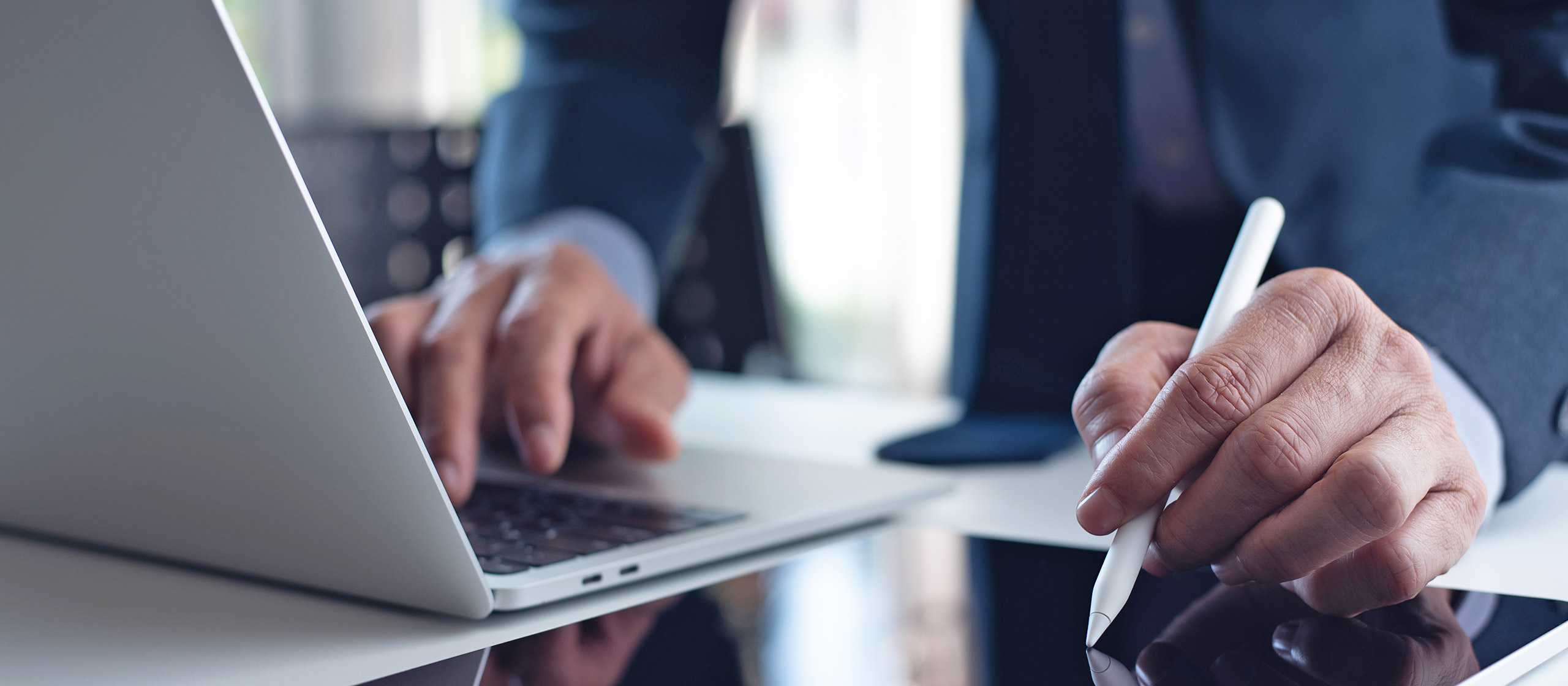 Una persona in giacca e cravatta sta digitando su un laptop e su in tablet