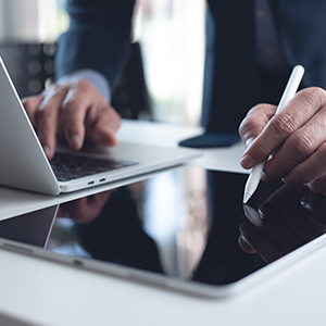 Una persona in giacca e cravatta sta digitando su un laptop e su in tablet